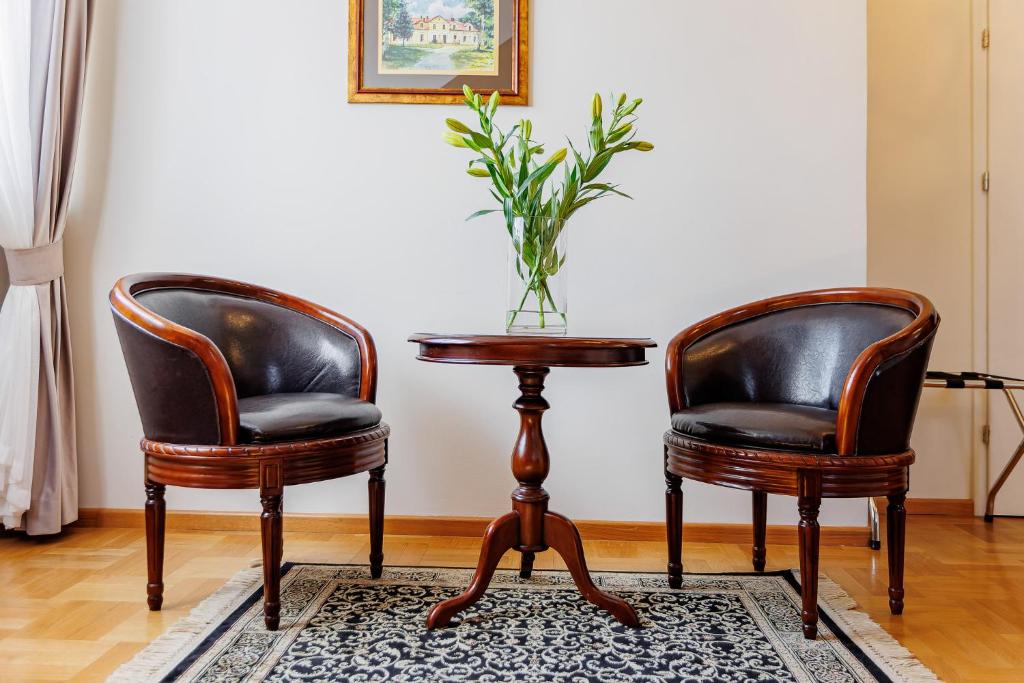 Pair of dark leather armchairs flanking small wooden table with glass vase of lilies, elegant rug.