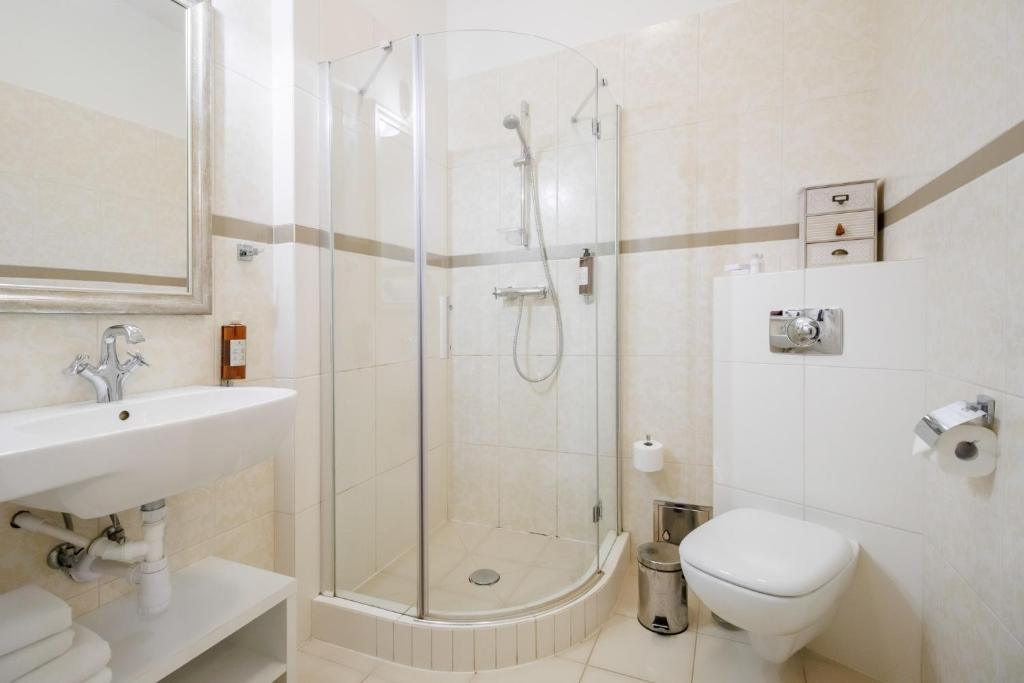 Clean tiled bathroom with glass corner shower, wall-mounted toilet, sink and toilet paper holder.