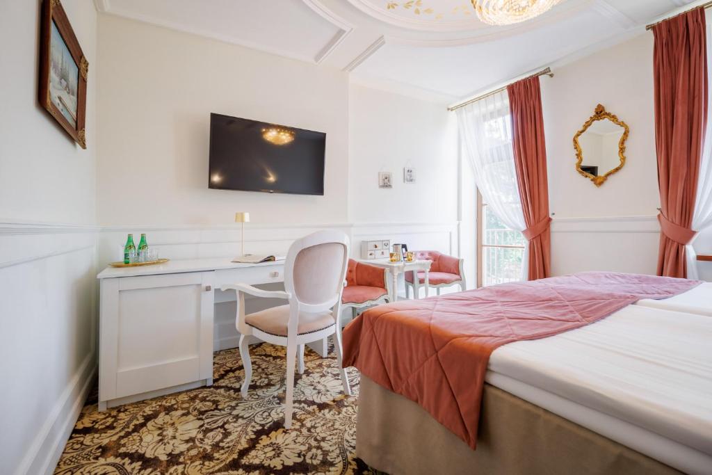 Bright hotel room with twin beds, coral throws, desk beneath TV and window with curtains.