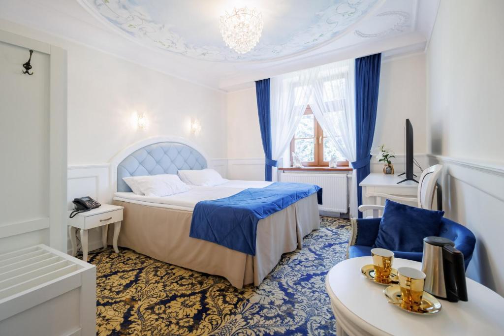 Elegant double bedroom with blue bed runners, chandelier, window drapes, seating area with gold cups.