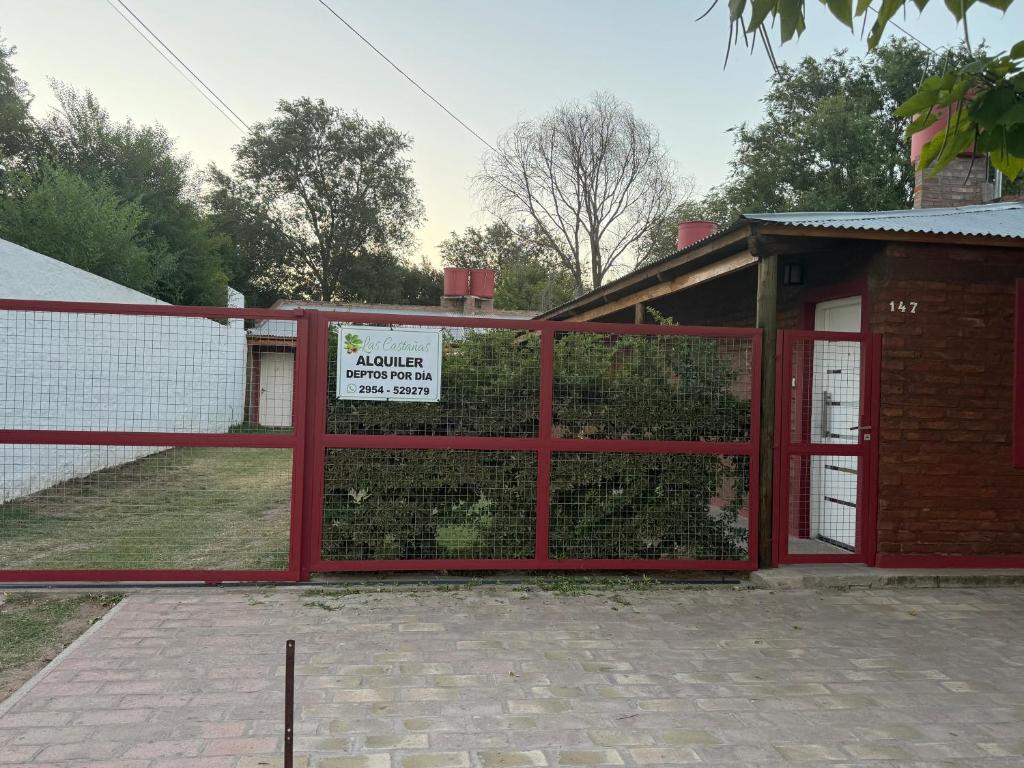 ein roter Zaun mit einem Tor und einer Hecke in der Unterkunft Las Castañas in General Acha