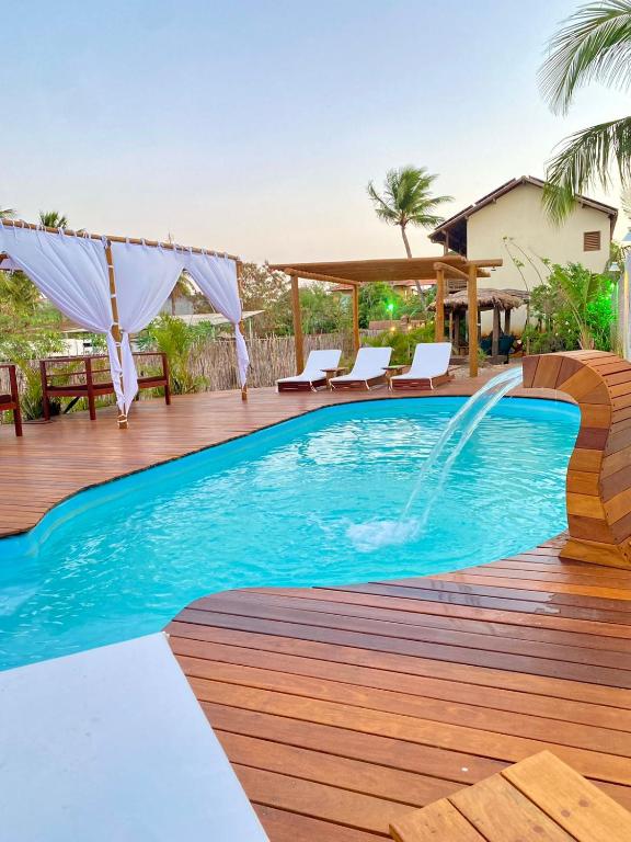 a pool with a wooden deck with chairs and a fountain at NaPraia Brasil Pousada in São Miguel do Gostoso