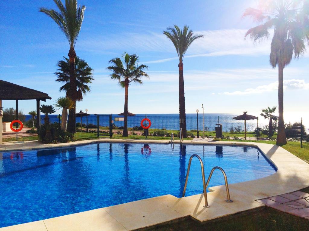 a swimming pool with palm trees and the ocean at Apartments Bermuda Beach in Estepona