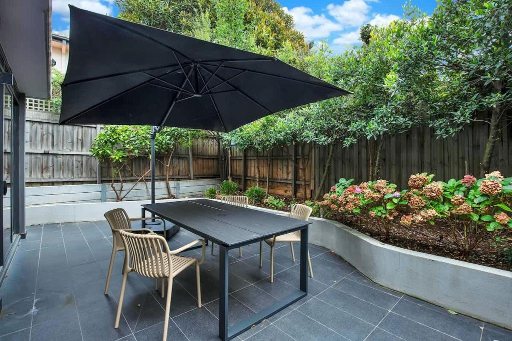 - une table noire avec des chaises et un parasol sur la terrasse dans l'établissement Canopy - Boutique Elwood Luxury with parking, à Melbourne
