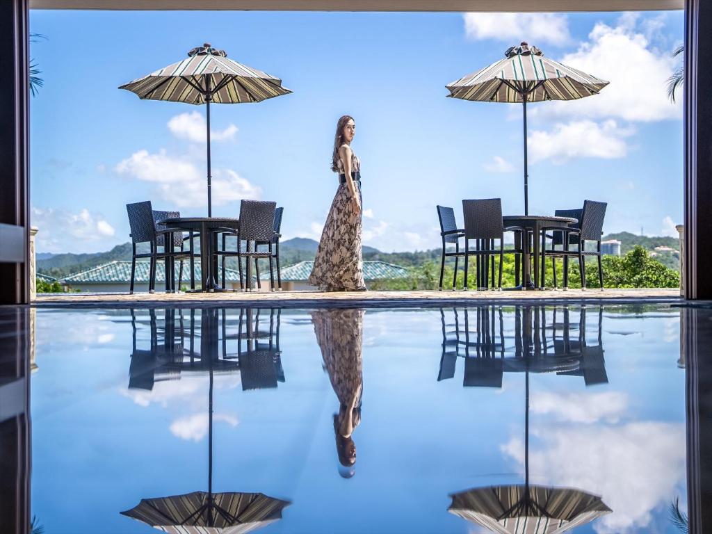 a woman walking next to a swimming pool with umbrellas at Oriental Hills Okinawa in Onna