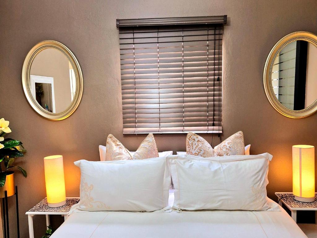 a bedroom with two mirrors and a bed with white pillows at URlyfstyle Cottage 10km from OR Tambo Int Airport in Kempton Park