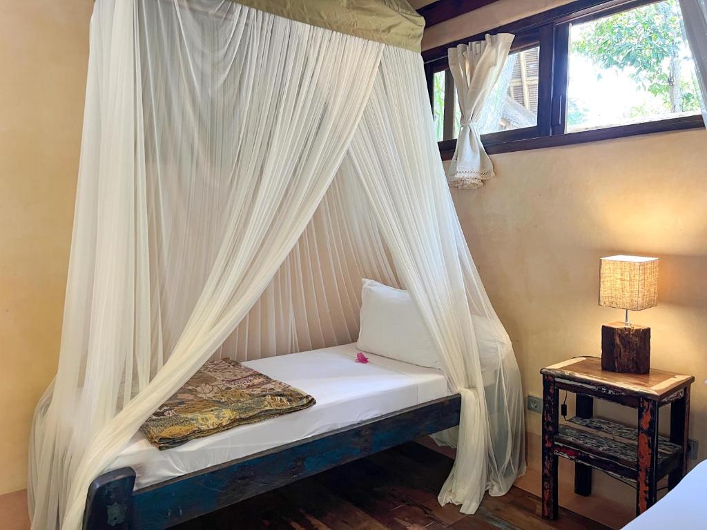a bedroom with a canopy bed with white curtains at Gili Asahan Eco Lodge & Restaurant in Gili Asahan