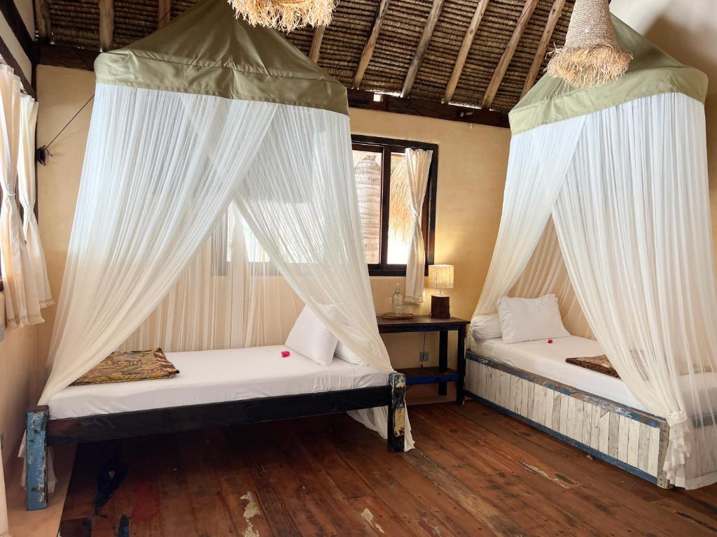 two beds in a room with white curtains at Gili Asahan Eco Lodge & Restaurant in Gili Asahan