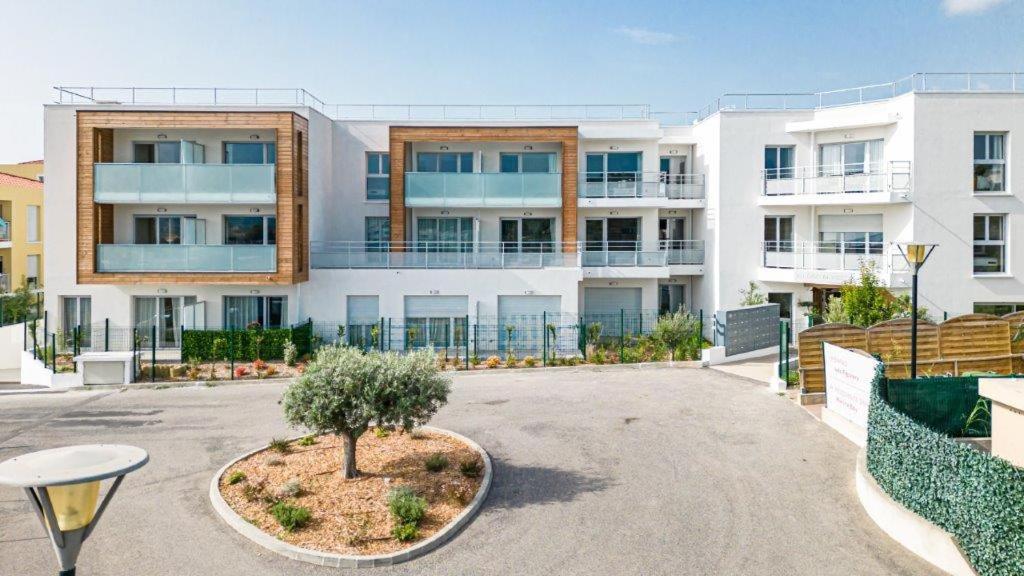 un grand bâtiment blanc avec un arbre dans une cour dans l'établissement Résidence Senior Marina Bay, à Villeneuve-Loubet
