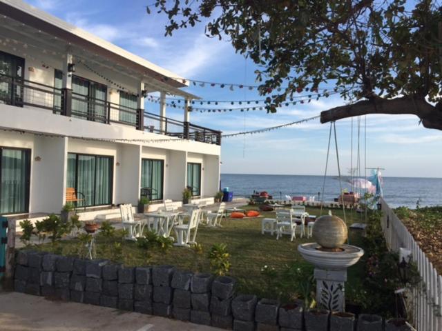 ein Gebäude mit einem Garten mit Tischen und Stühlen und dem Meer in der Unterkunft Kodtalay Resort in Chao Lao Beach