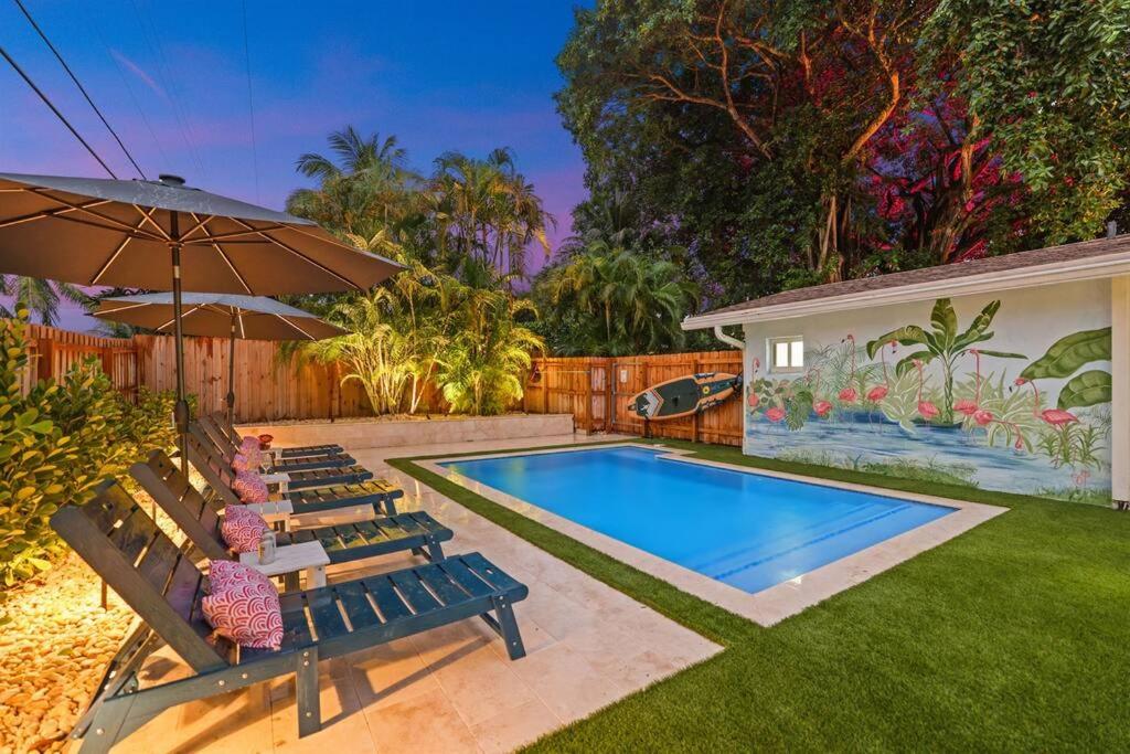 a backyard with a swimming pool with benches and an umbrella at Flamingo Palms in Delray Beach