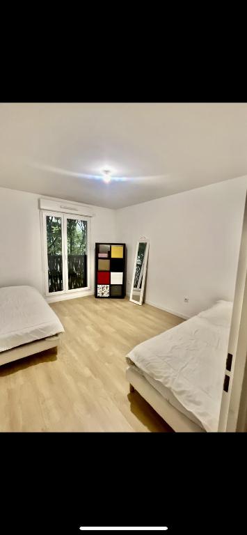 Cette chambre blanche dispose de deux lits et d'une fenêtre. dans l'établissement Chambre confortable à 25min de Paris, à Villemomble