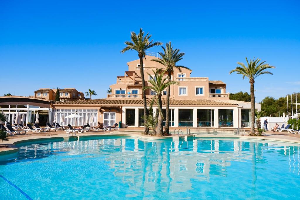 ein Swimmingpool vor einem Haus mit Palmen in der Unterkunft Aparthotel Ciudad Laurel in Cala Millor