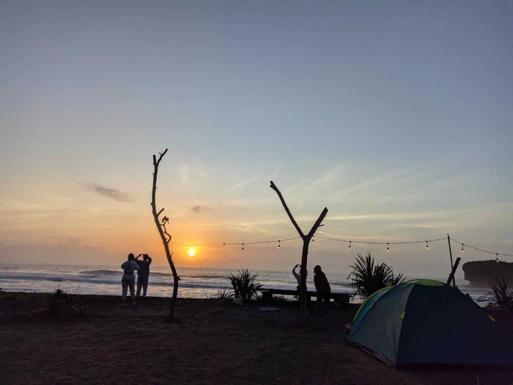 eine Gruppe von Menschen steht um ein Zelt am Strand in der Unterkunft Tenda camping in Madasari