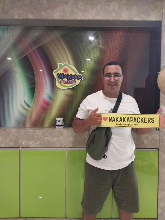 a man holding a sign in front of a tv at WakakaPackers in Kuala Lumpur
