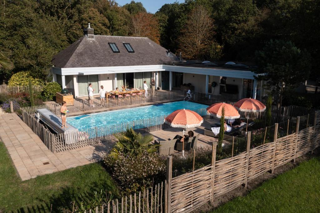 a swimming pool in front of a house with umbrellas at Villa met privézwembad, 10 minuten van het strand in Noordwelle