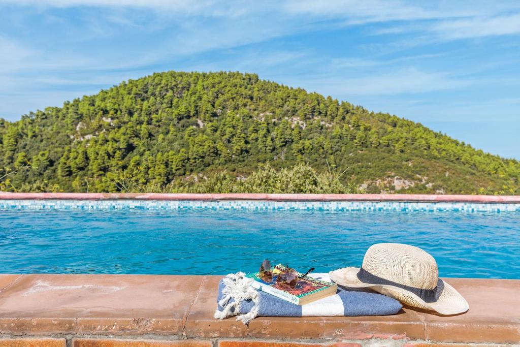 a hat and a book next to a swimming pool at Sirens Villas in Skopelos Town