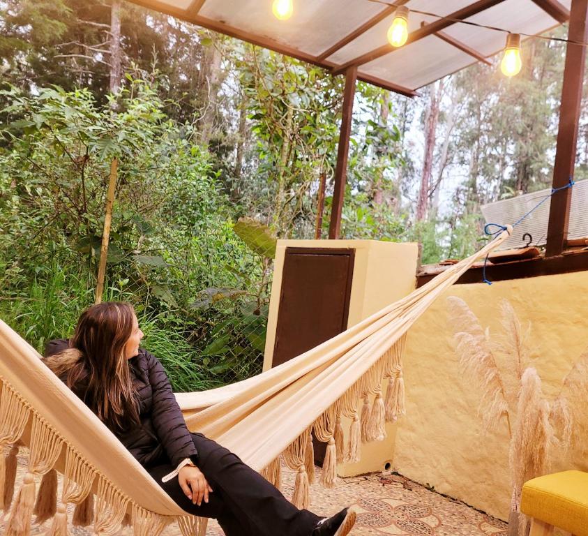 une femme assise dans un hamac sur une scène dans l'établissement La Pascana Ecolodge APTO BARRANQUERO frente al parque Arví Entorno natural excepcional, reserva natural, áreas protegidas, conexión con la naturaleza y avistamiento de aves a 3km del metrocable Guarne, à Guarne