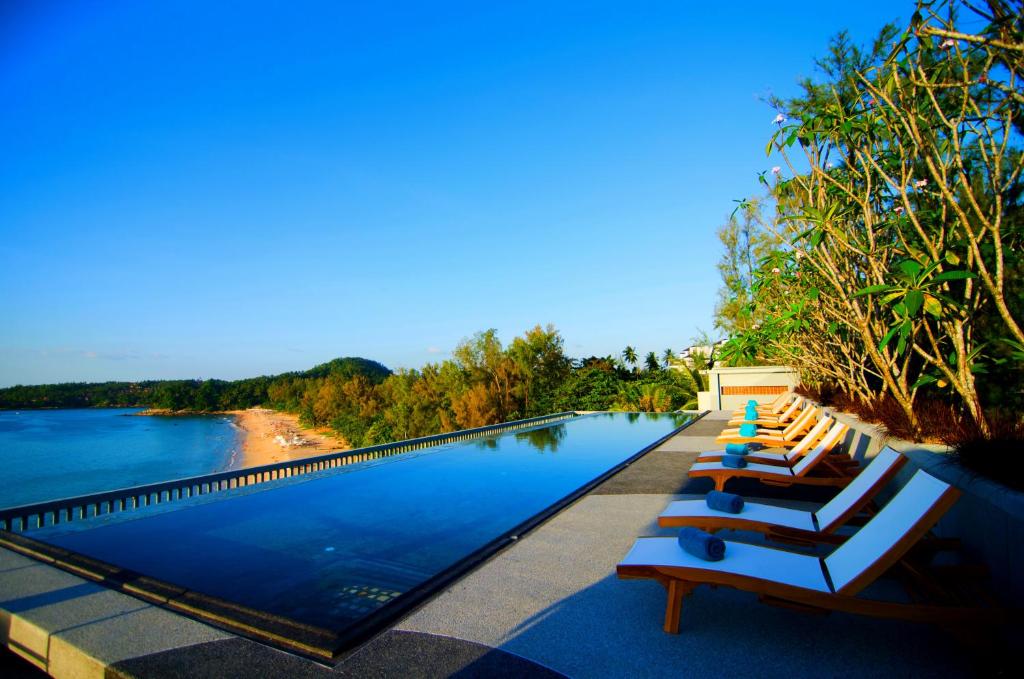 a pool with lounge chairs next to a body of water at Norn Talay Surin Beach Phuket in Surin Beach