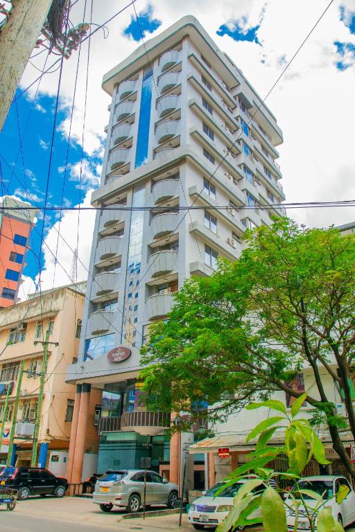 a tall white building with cars parked in front of it at Sleep Inn Hotel - City Centre in Dar es Salaam