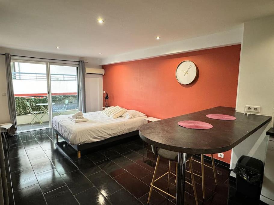 - une chambre avec un lit, une table et une horloge dans l'établissement Grand Studio Centre Cannes, à Cannes