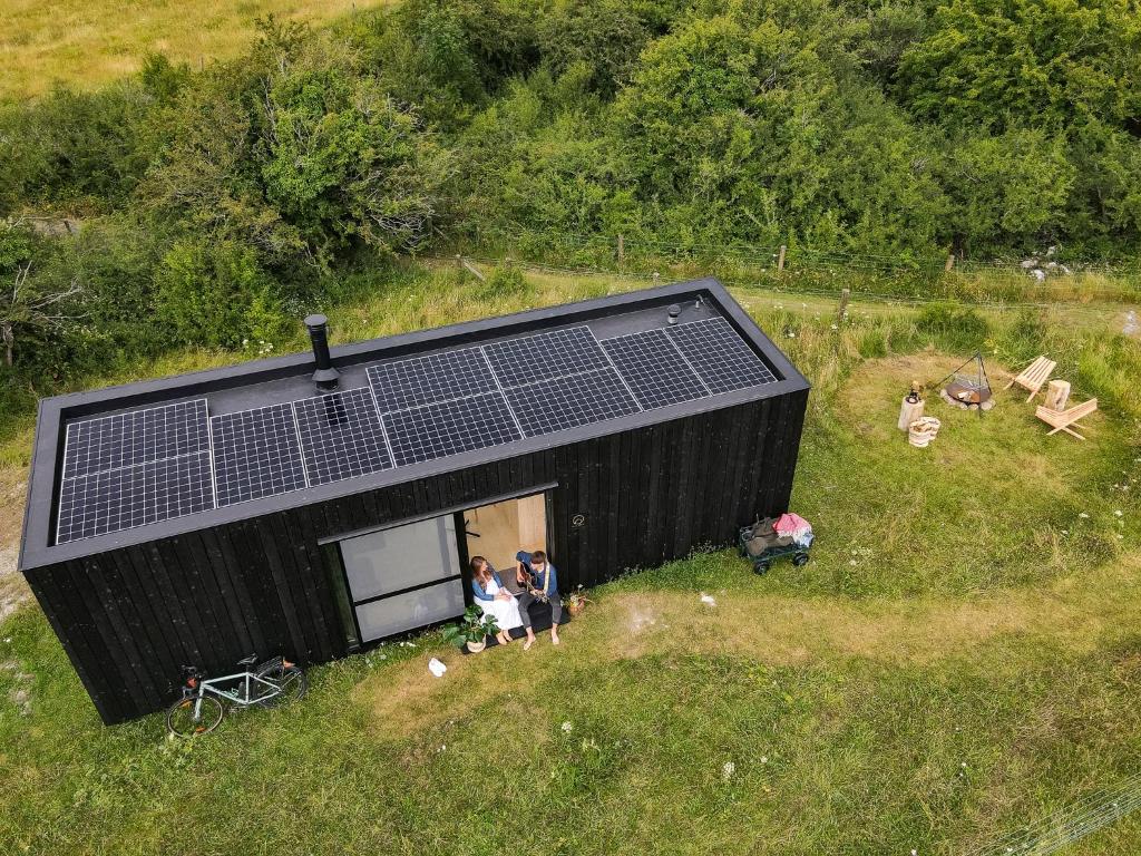 due persone in piedi fuori da una casa nera con pannelli solari sopra. di Wild Cabins Kinvara a Cloonnasee
