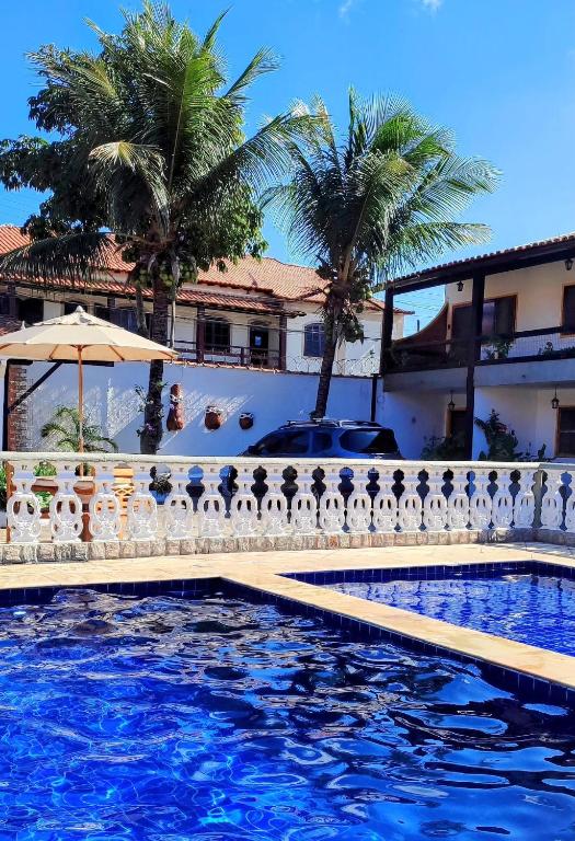 a pool in front of a house with palm trees at Refúgio Peró - Praia, piscina e churrasqueira in Cabo Frio