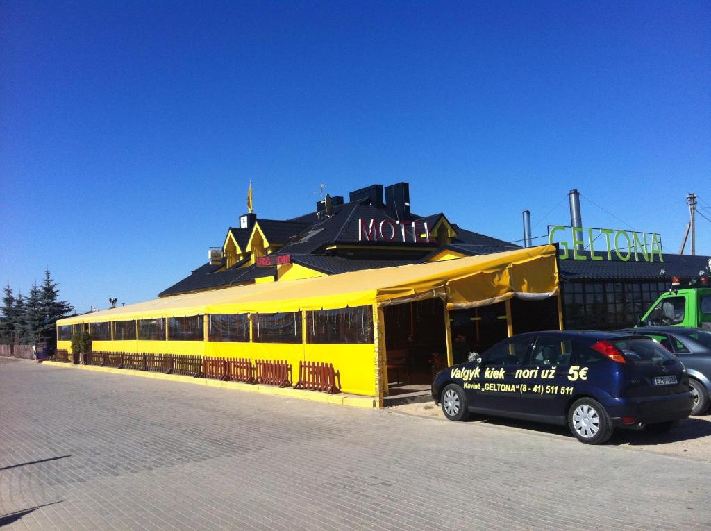 un edificio amarillo con un coche aparcado delante de él en Geltona en Šiauliai