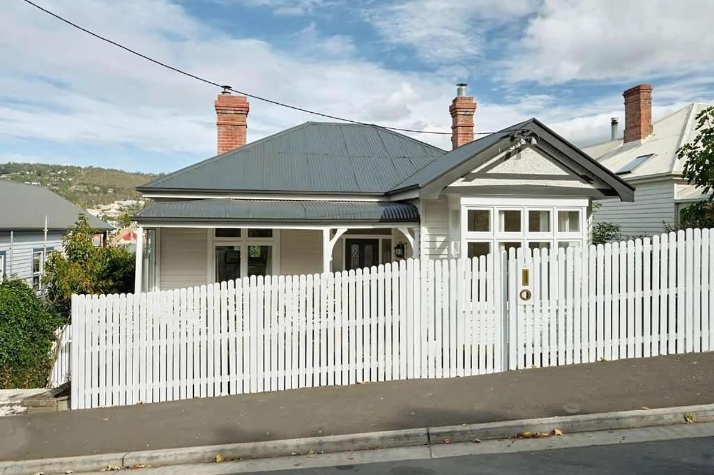 a white fence in front of a white house at Sunny spacious three bedroom apartment with views in Hobart