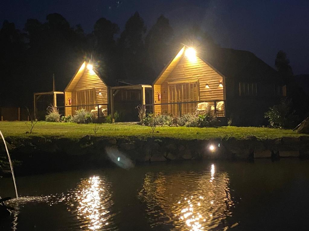 Dos cabañas de madera con luces sobre el agua por la noche en Cabana I com Banheira Hidro e Lareira - Chalet Mont Blanc - Urubici, en Urubici