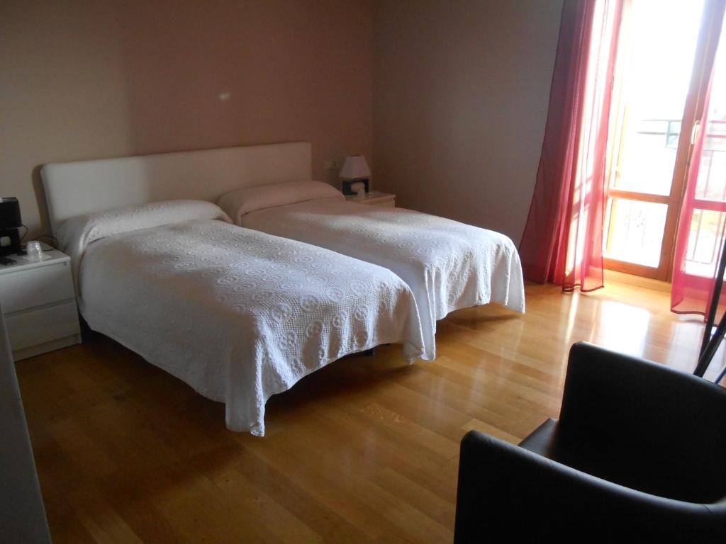 a bedroom with two beds with white sheets and a chair at Hospedaje Nuestra Señora de Ujue in Tafalla