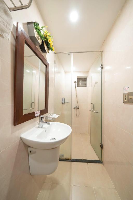 A narrow bathroom with a pedestal sink and fully enclosed glass shower.