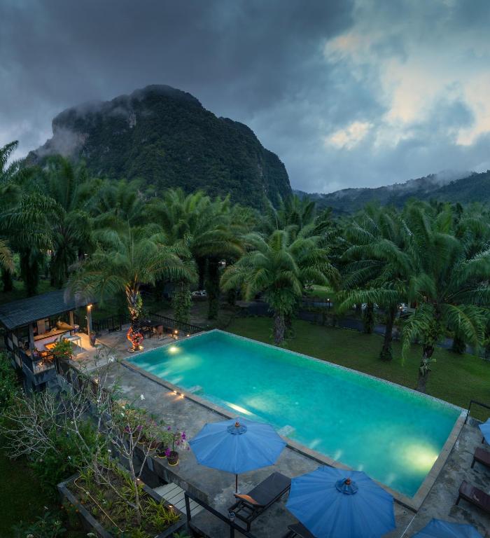 a pool with umbrellas and a mountain in the background at Krabi Green Hill Pool Villas in Ban Nong Thale