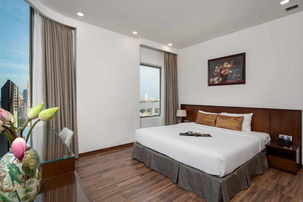 A bright double room with a polished wood floor, framed artwork, and city-and-water views through tall windows.