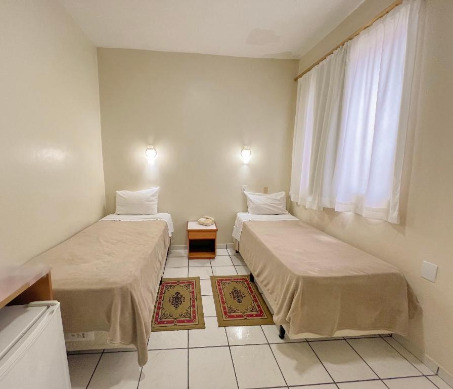two beds in a room with a window at Hotel Ibiá in Montenegro
