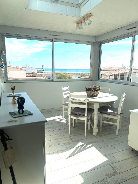une cuisine avec une table, des chaises et des fenêtres dans l'établissement Le Soulairol Bleu, à Leucate