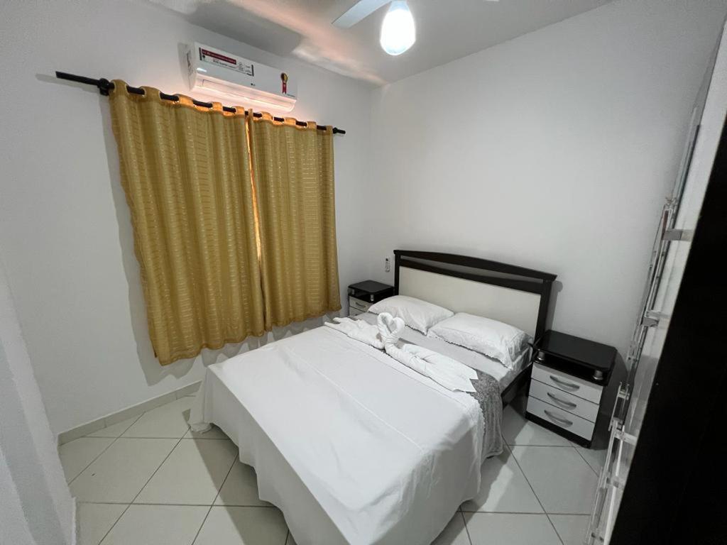 a bedroom with a white bed and a yellow curtain at MELHOR ESCOLHA - 2 Quartos com AR CONDICIONADOS SPLIT, Air Fryer, Wi-Fi, Disney Plus, Star Plus, HBO Max, Cadeiras de Praia, Caixa Térmica - 7 pessoas - Localização Nobre - CONFORTO Máximo! in Guarapari