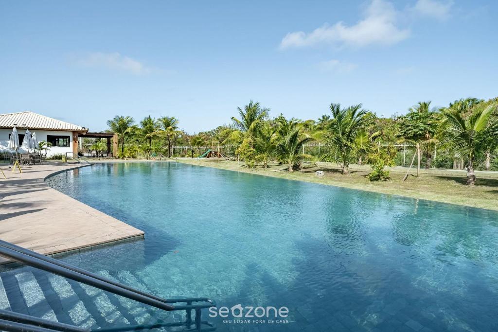 a swimming pool with blue water and palm trees at VLP - Apartamentos próximos à Praia do Forte/BA in Mata de Sao Joao