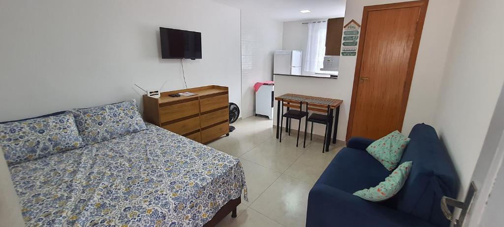 a bedroom with a bed and a chair and a kitchen at Apartamento Extensão do Bosque in Rio das Ostras