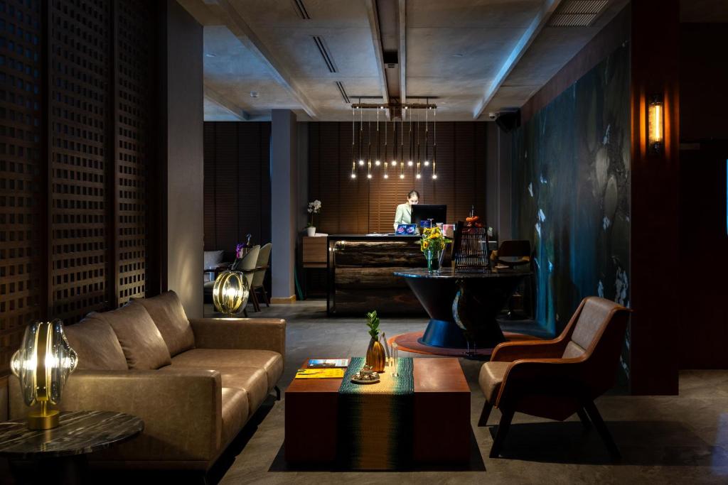 A dark, design-led lobby lounge pairs a sofa and armchairs with a reception desk beyond.