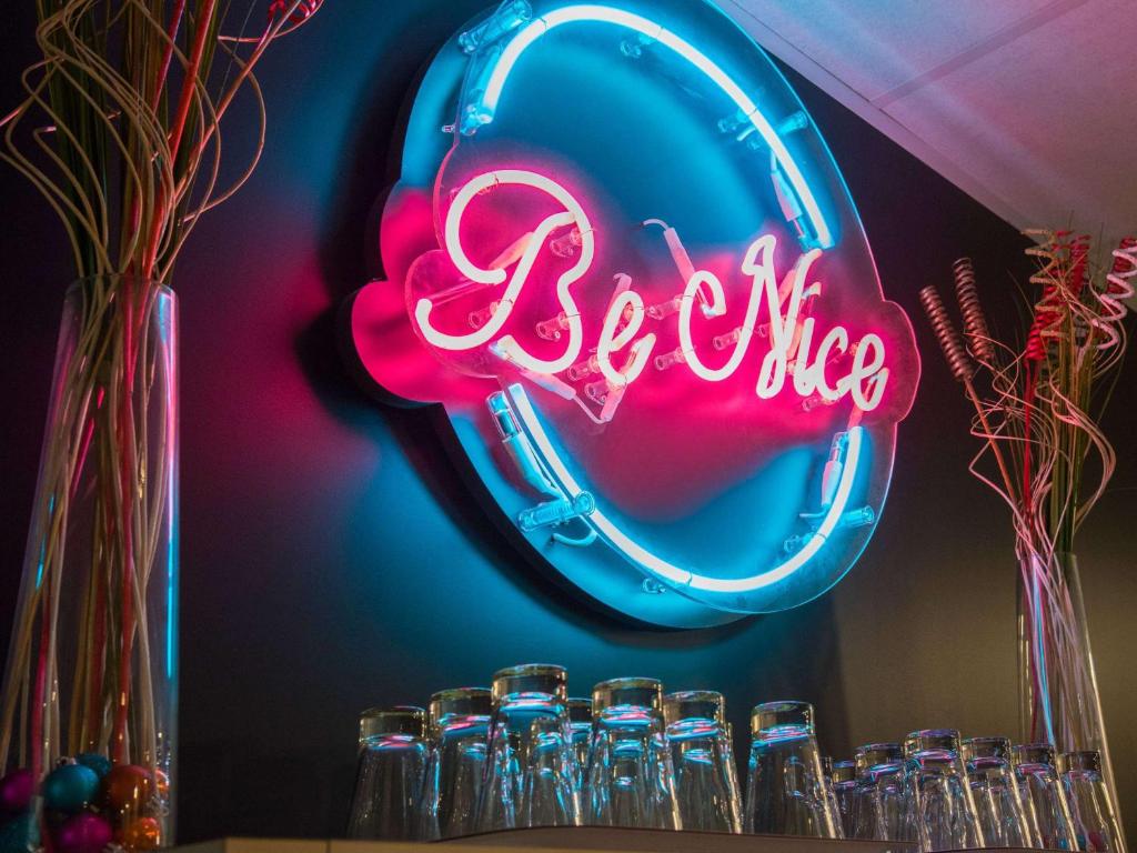 a neon sign that says be nice next to glasses at Ibis Styles Nice Centre Gare in Nice