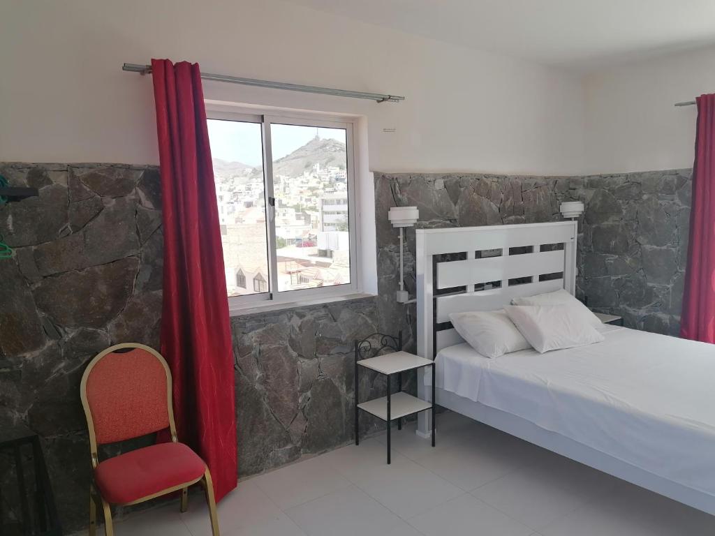 a bedroom with a bed and a window and a chair at STUDIO VUE MER - CASA da LUZ in Mindelo