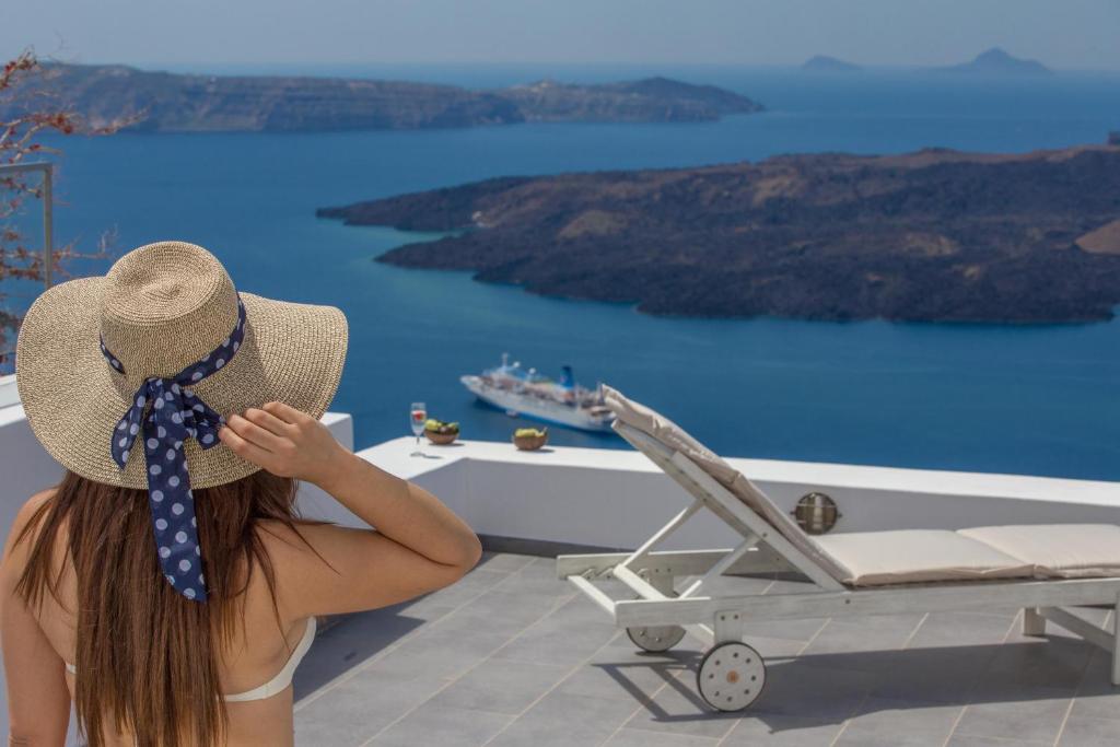 Una chica con sombrero sentada en un balcón mirando el agua en Karpimo Horizon en Firostefani