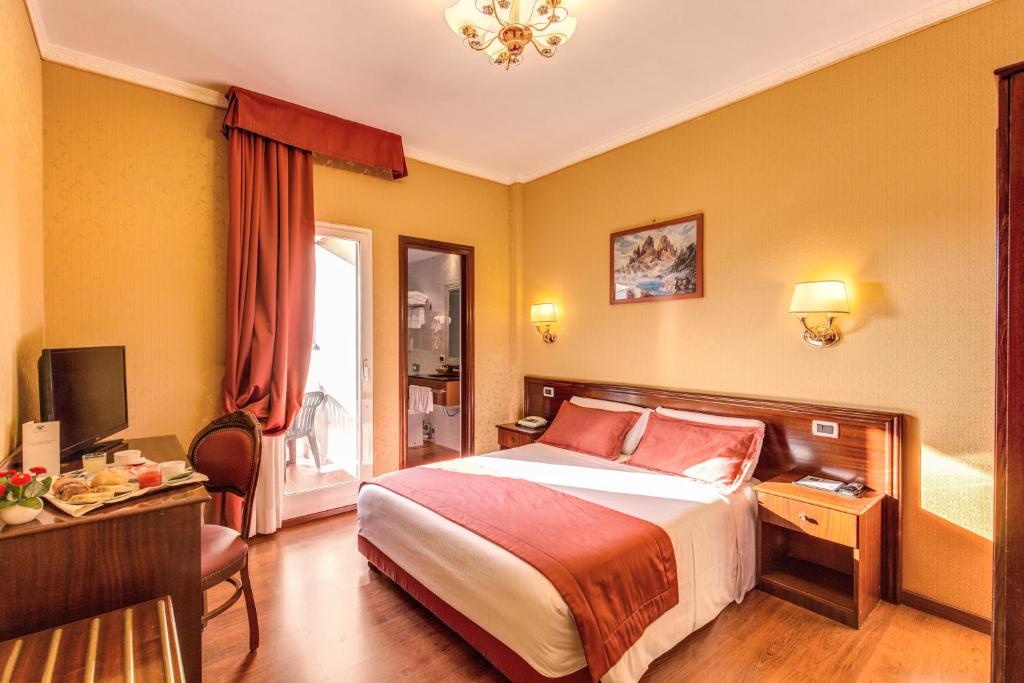 ローマにあるホテル インペロのベッド、デスク、テレビが備わるホテルルームです。