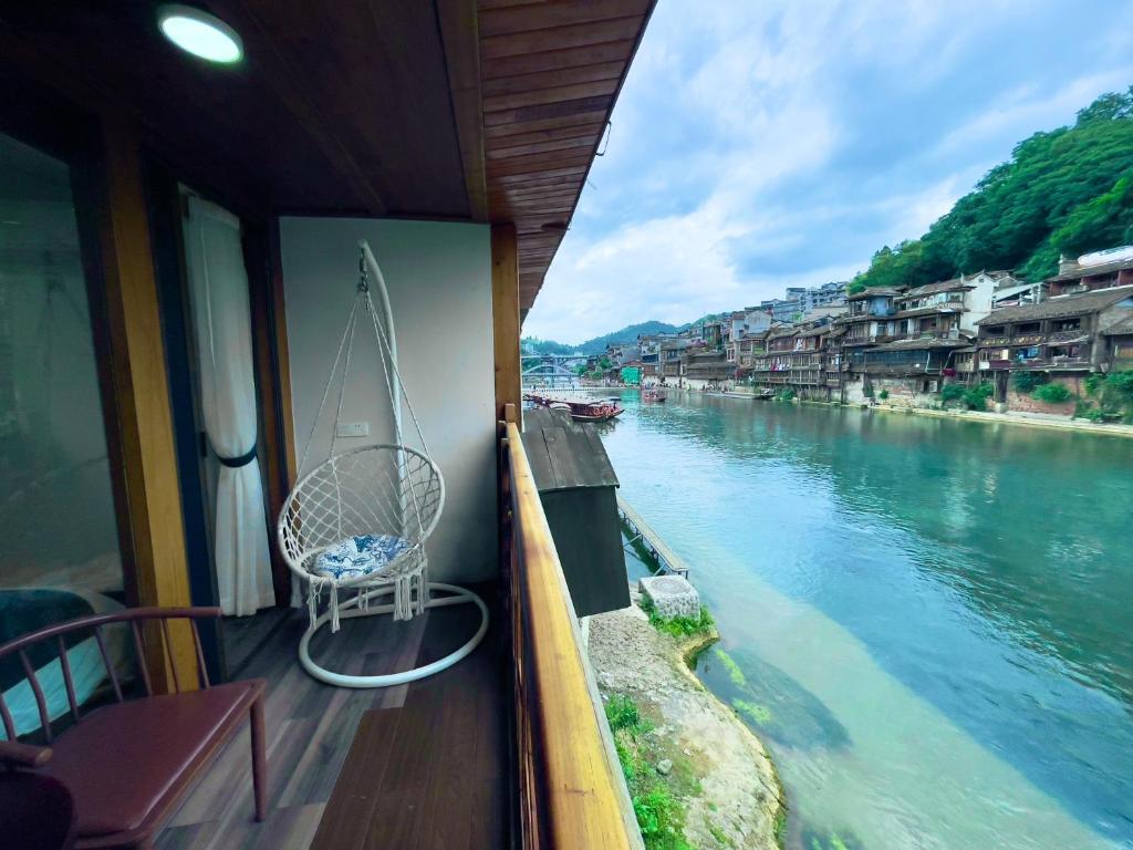 a chair on a balcony looking out over a river at Bian Cheng Xing Zi Inn in Fenghuang County