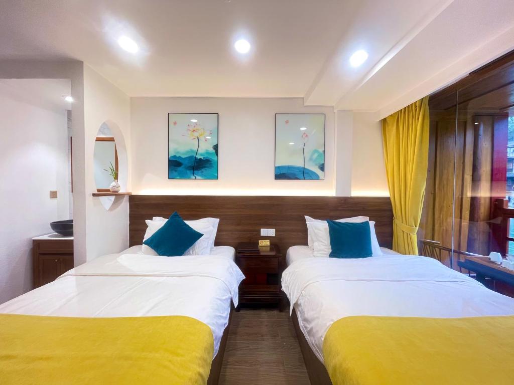 two beds in a hotel room with yellow and blue pillows at Bian Cheng Xing Zi Inn in Fenghuang County