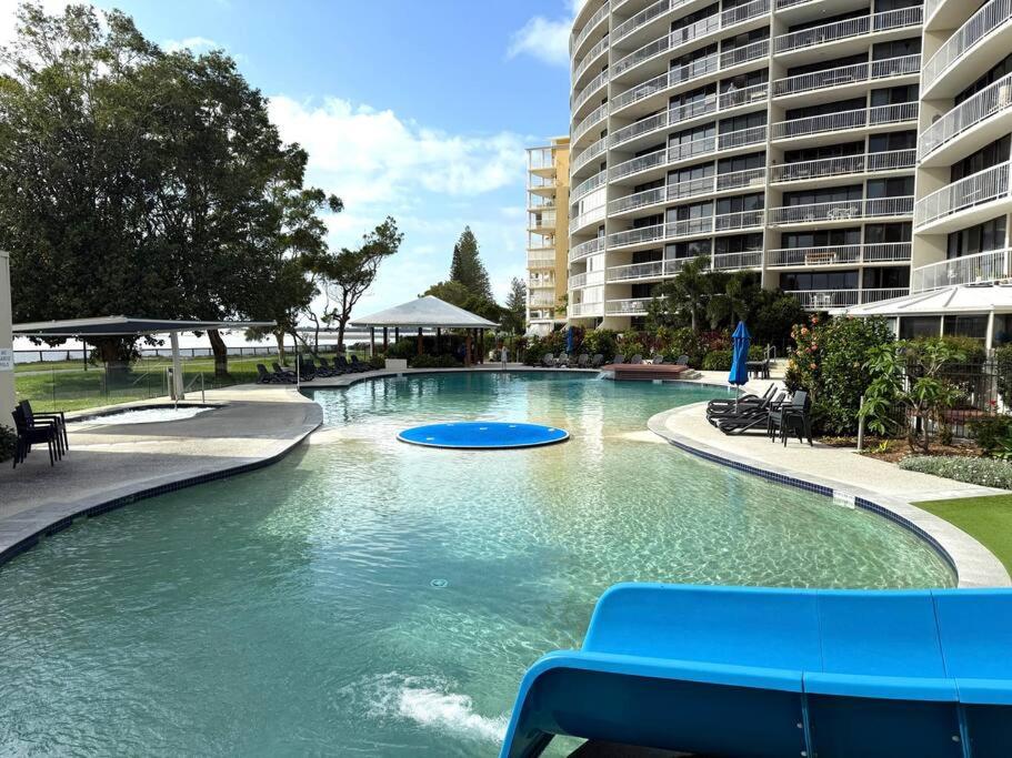 a swimming pool with a blue bench in front of a building at Gemini Resort, 2bedroom Unit19 and carpark Golden Beach, Caloundra in Golden Beach