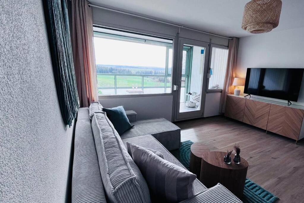 un salon avec un canapé et une grande fenêtre dans l'établissement Apartment mit Wintergarten & Grüner Aussicht im Schwarzwald, à Löffingen