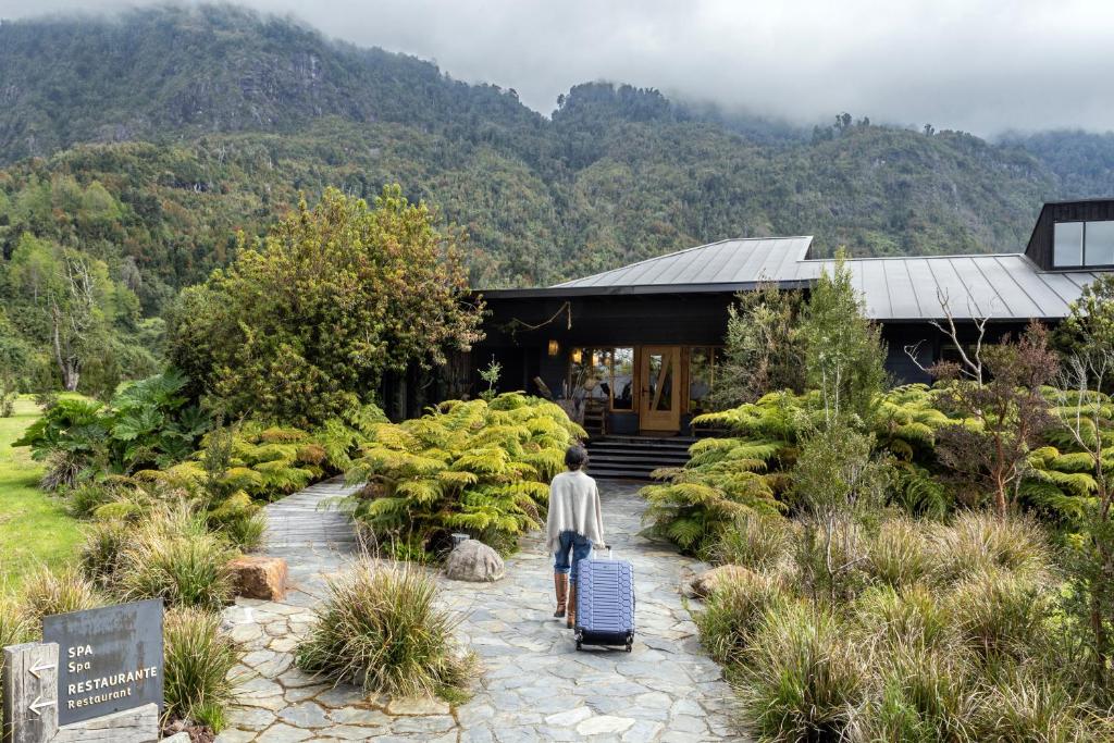 a man walking with luggage in front of a building at Futangue Hotel & Spa in Lago Ranco