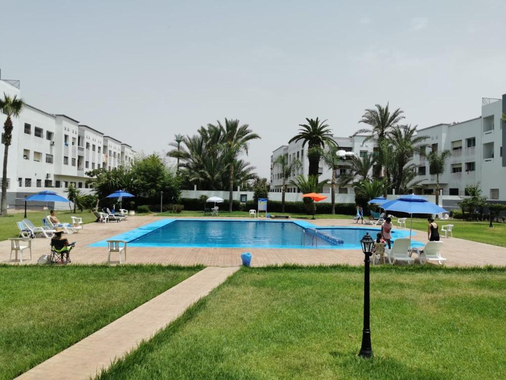 穆罕默迪耶Appartement corniche d'or, Mohammedia的一座建筑物附近，游泳池里有人坐在遮阳伞下。